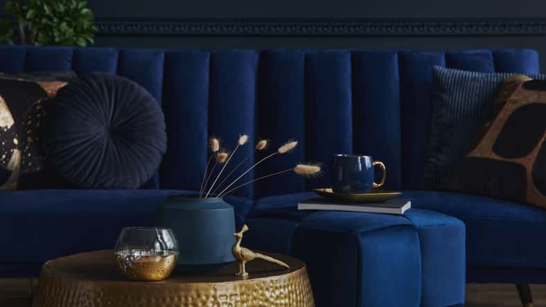 Stylish and elegant details in the glamour living room interior. Golden metal coffee table and creative personal accesories. Dark blue sofa on the background. Template. Copy space.