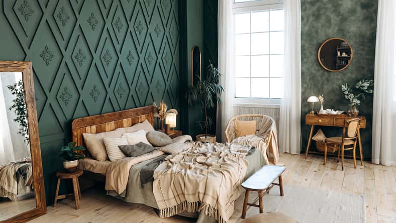 Cozy boho bedroom with wooden furniture, console table, textiles, green walls, large windows and potted plants. Empty space