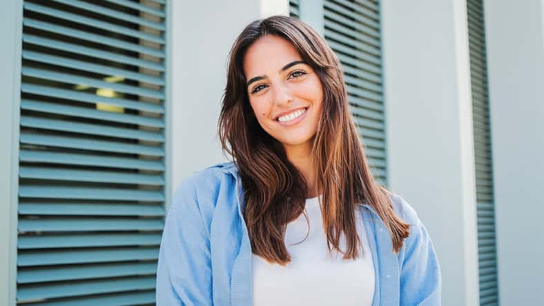 Happy caucasian young student female looking at camera enjoying with a perfect white teeth. Portrait of a joyful and adorable teenage brunette woman posing for a college promotion with crossed arms. High quality photo