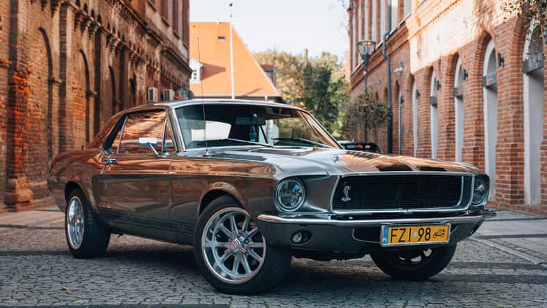 Vintage Ford Mustang GT 1967 estacionó en el medio de Industrial Road en un día soleado. Diseño americano con llantas de aleación. Perfecto para artículos de marketing, publicidad o prensa.