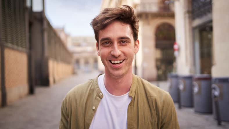 Close up portrait of happy young European man happy smiling face on street. Male people with cheerful expression looking at camera in open air. Nice boy posing for photo outdoor.