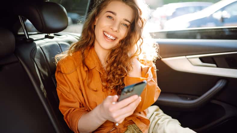 Young woman uses a smartphone while sitting in the back seat of a car. Concept of technology, traveling by car, business.