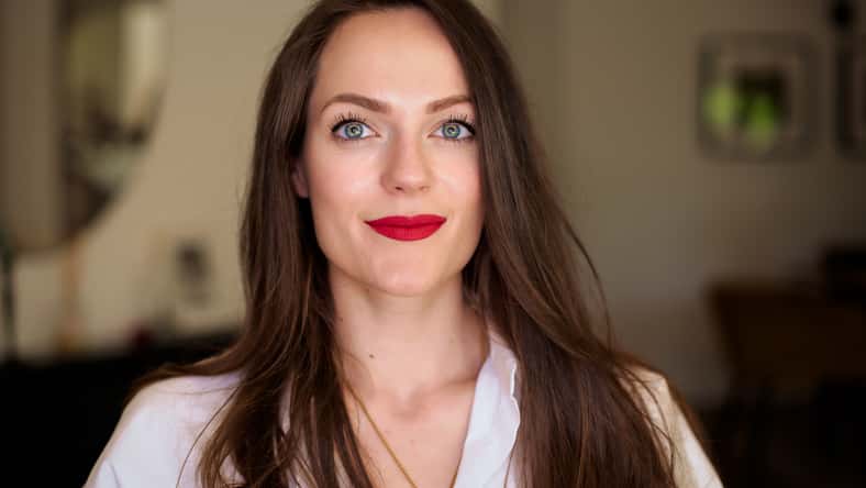 Close-up portrait of smiling young woman with green eyes. Brunette haired female wearing red lipstick and white shirt.