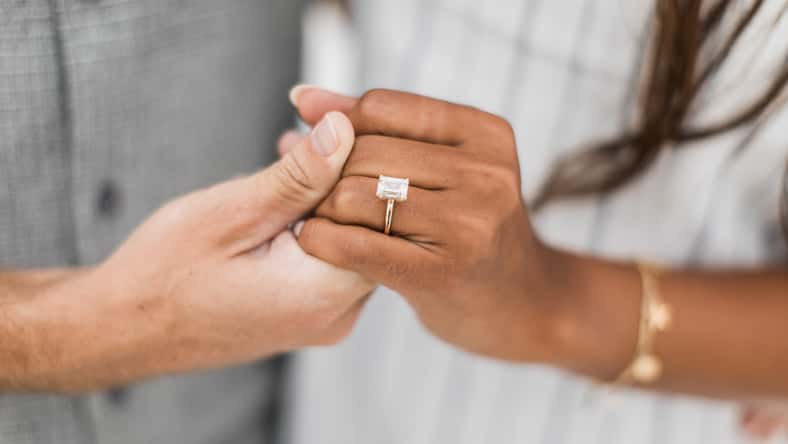 woman and man holding hands while displaying their proposal diamond ring