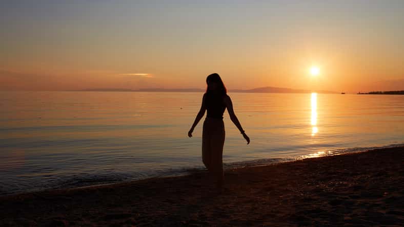 A pretty girl enjoys the sunset on a sandy beach. Summer travel, vacations at sea.