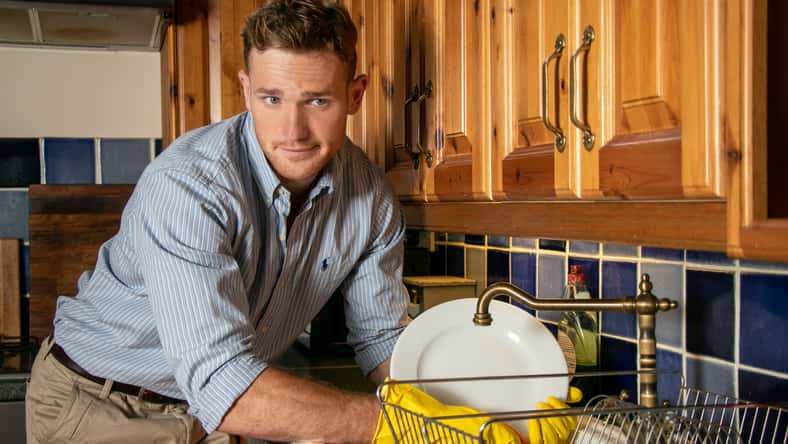 Good looking unhappy man washing plates and smiling