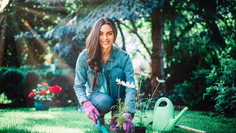 Disparo completo de la jardinería de mujeres jóvenes en casa en el patio trasero. Mujer feliz con ropa casual mientras planta flores.