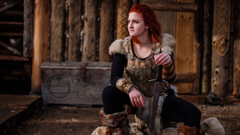 La mujer pelirroja es una vikinga. En el contexto de un pueblo o un asentamiento antiguo. En manos de una espada