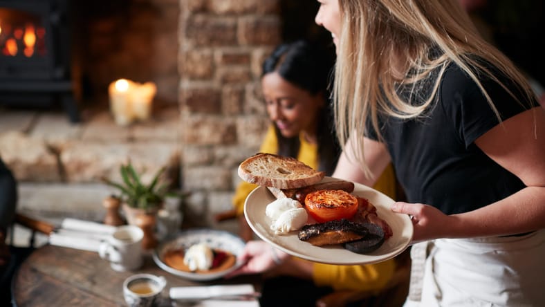 Primer plano de camarera trabajando en un pub inglés tradicional que sirve desayuno a los invitados