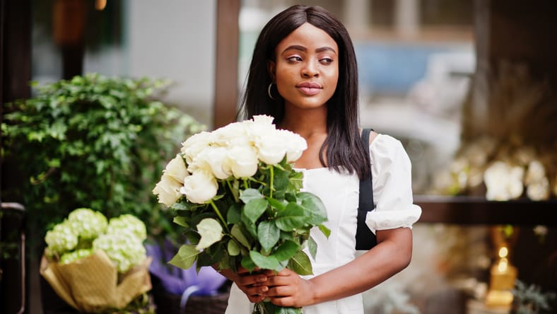 Hermosa chica afroamericana que sostiene un ramo de flores de rosas blancas en las citas en la ciudad. La empresaria negra con un montón de flores.