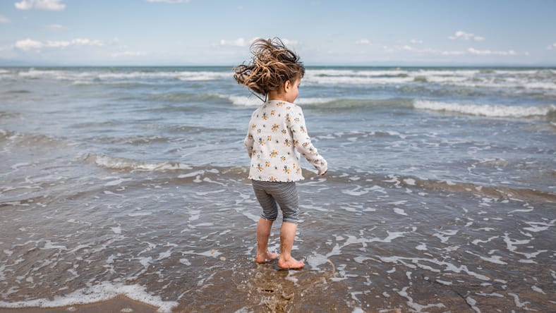 Vista trasera de la niña con el pelo soplado jugando con olas en el mar
