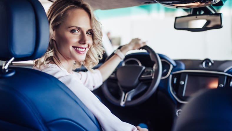 Retrato de una mujer joven sonriente sentada en el auto y mirando la cámara