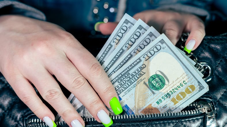 La mujer saca dinero de una elegante bolsa de cuero. Una mujer pone dólares en su bolso