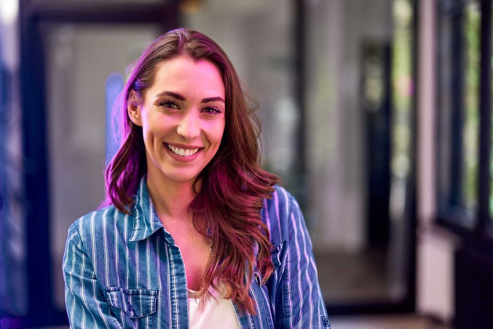 A happy female employee on her first work day, standing at the workplace and smiling for the camera.