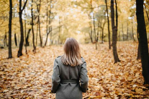 a woman walking down a road covered with fallen leaves