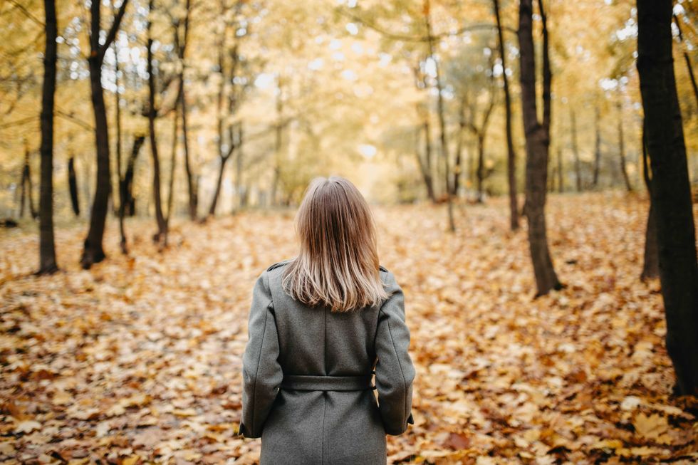 a woman walking down a road covered with fallen leaves