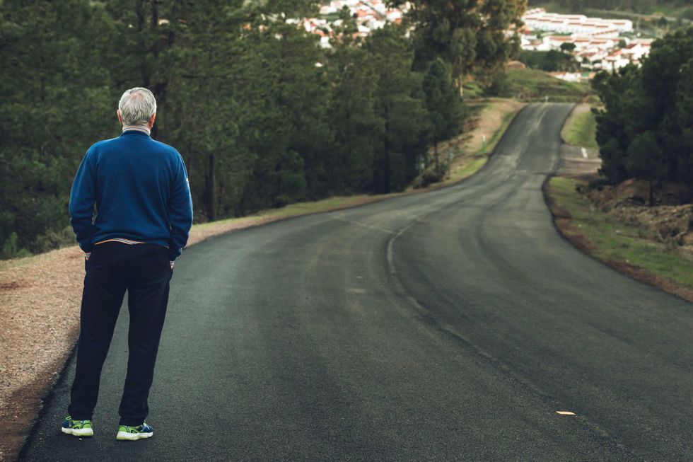 Active senior man standing on lonely road between mountains. Older man of back standing on lonely highway