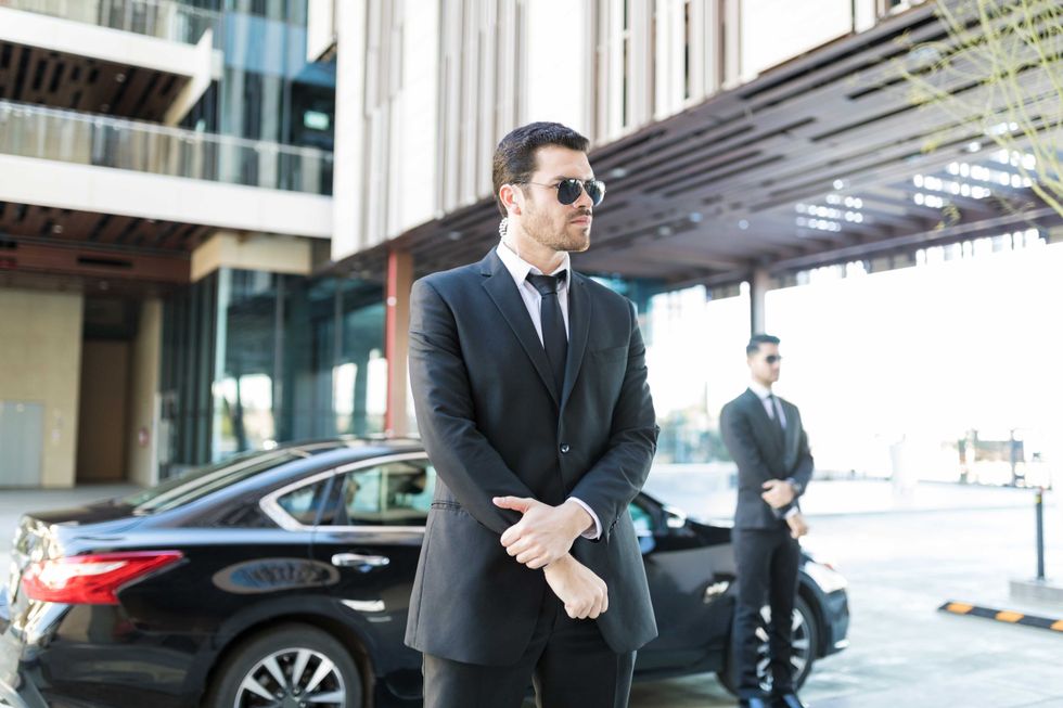 Alert bodyguard keeping an eye on surroundings with car parked on city street
