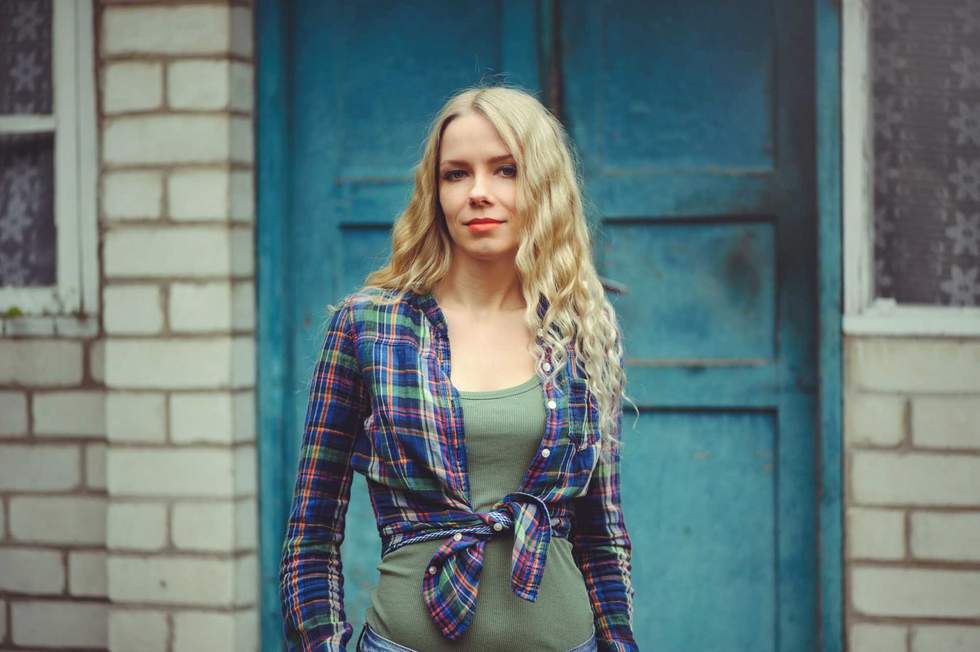 attractive blonde girl on the background of an old house, dressed in jeans and shirts.