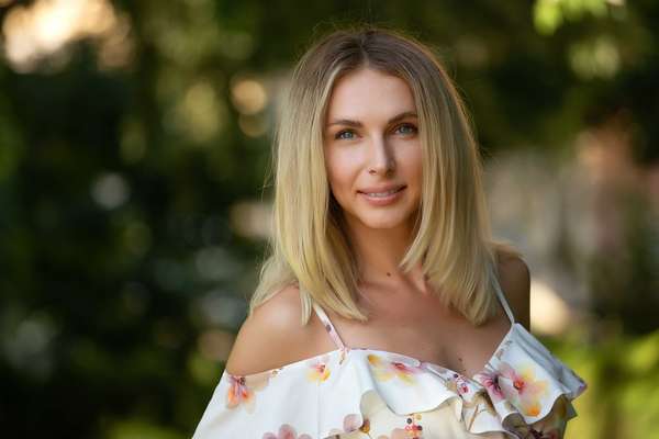 Attractive young blonde woman in a light summer dress with flowers