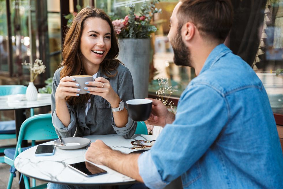 Attractive young couple in love having lunch while sitting at the cafe table outdoors, drinking coffee, talking