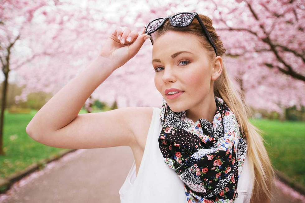 Attractive young female model posing at spring park. Casual young woman wearing sunglasses and scarf looking at camera.