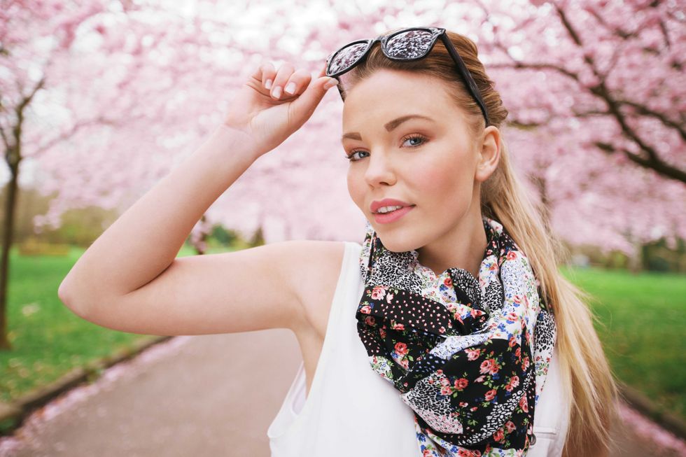 Attractive young female model posing at spring park. Casual young woman wearing sunglasses and scarf looking at camera.
