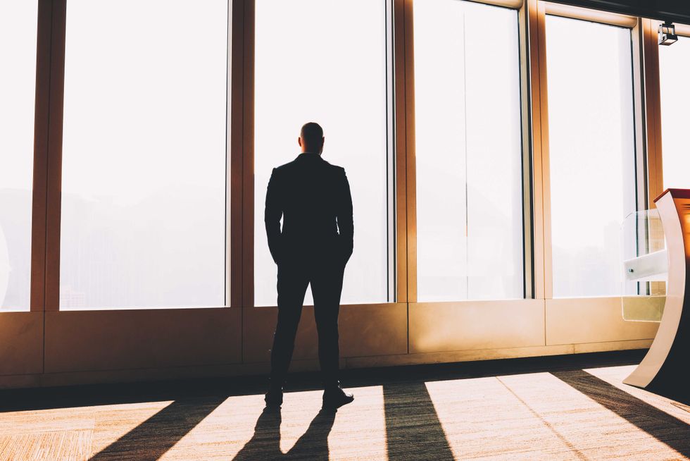 Back view of businessman dressed in formal clothes and holding hands in pockets while thinking on creative ideas for developing own company and financial profit while enjoying sunset scenery