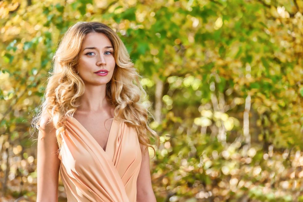 Beautiful blonde girl close up portrait. Blue eyes, curled hair. Autumn background