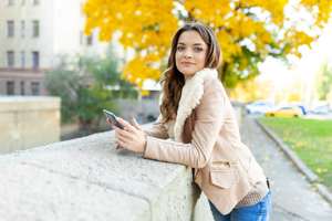 Beautiful brunette girl standing warm autumn day with background of trees with yellow foliage and a city