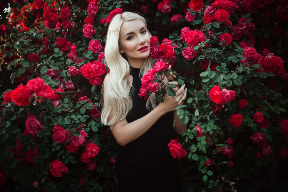 Beautiful smiling blonde woman in bush of red roses