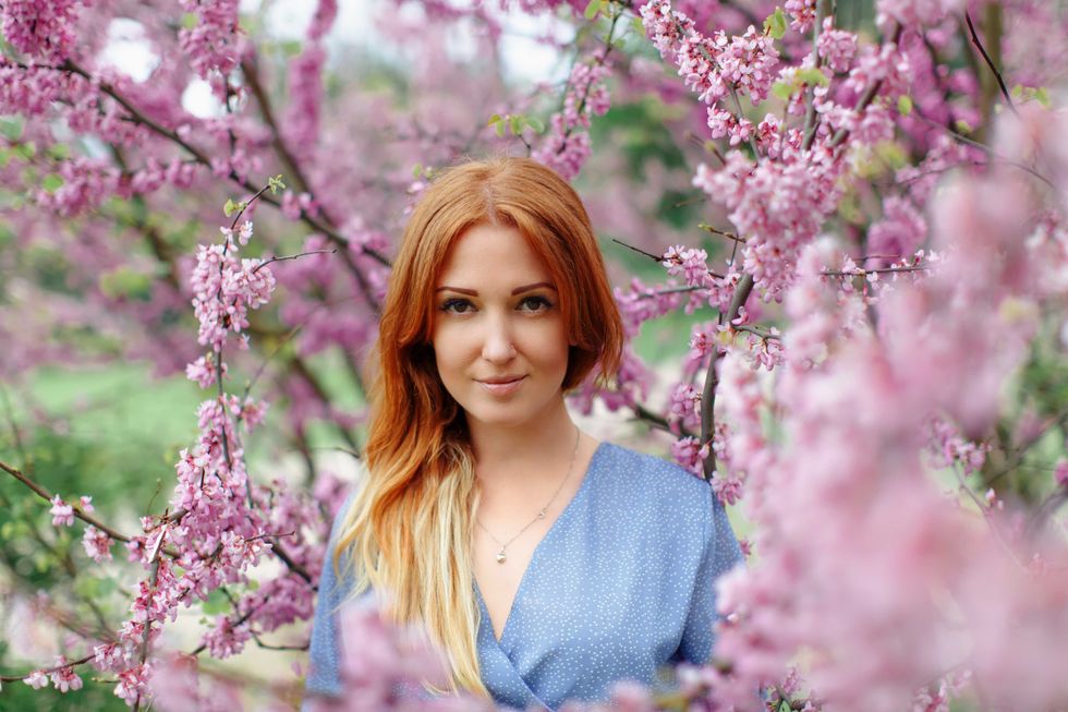 Beautiful smilling redhead woman in spring time blossom cherrytrees garden. Perfect time for a walk. Enjoy the spring and sunny day. Social media, beauty, blogger, vlogger.