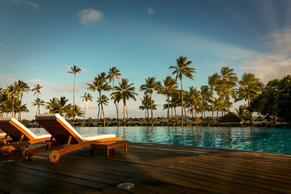 Beautiful tropical beach front hotel resort with swimming pool, sun-loungers and palm trees during a warm sunny day, paradise destination for vacations in Praia do forte, Bahia, Brazil.