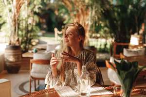 Beautiful young lady drinking water in restaurant, looking in the window, waiting for order. Summer cafe outdoor terrace