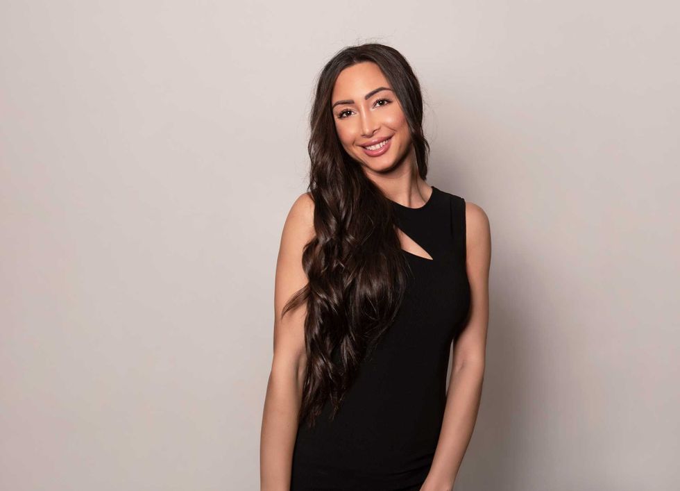 Beautiful young woman with long shiny black hair and natural make-up posing in dress on grey background