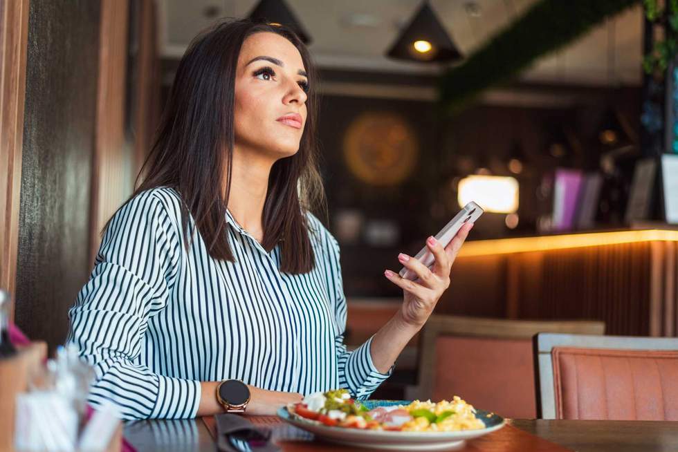 Businesswoman is holding a smartphone and looking up while waiting in a restaurant