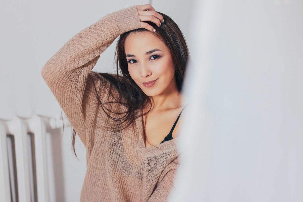 Candid portrait of smiling asian girl young woman with dark long hair in beige sweater on white curtain background