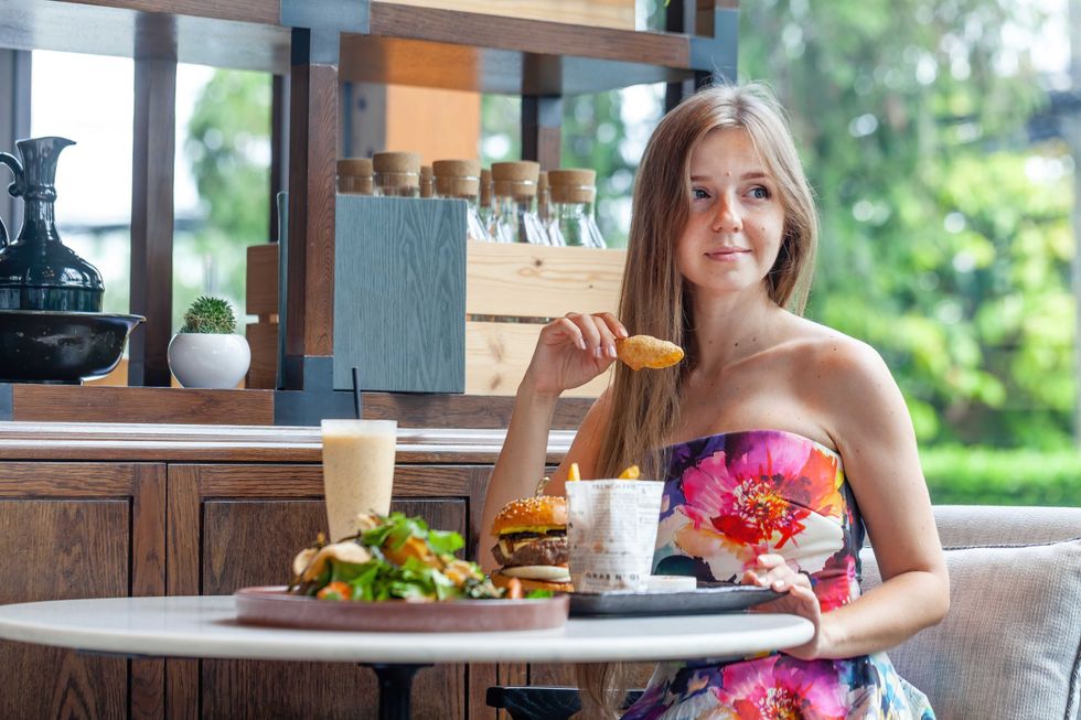 Casual lunch setting with delighted woman, vibrant dress, indulging in burger and salad, serene restaurant environment. Everyday healthy eating.