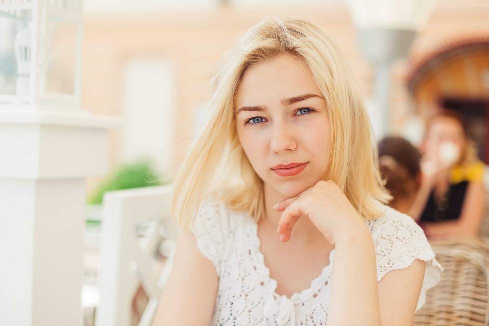 Close up portrait of toyng blondie girl sitting in outdoor cafe in summer. Leisure summer time and lifestyle of student girl