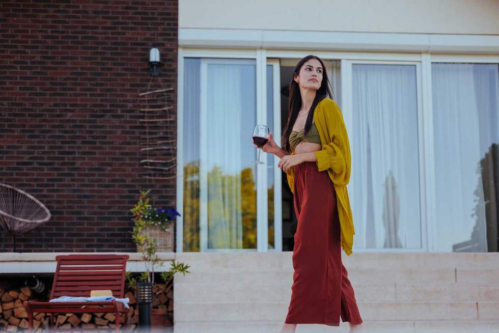 Elegant woman holding a glass of wine, experiencing solitude outside a house