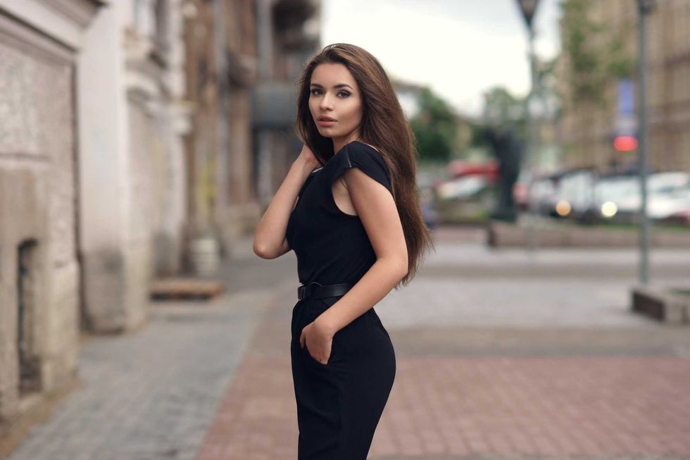 Fashion style portrait of young beautiful elegant woman in black dress walking at city streets on a windy dull day.