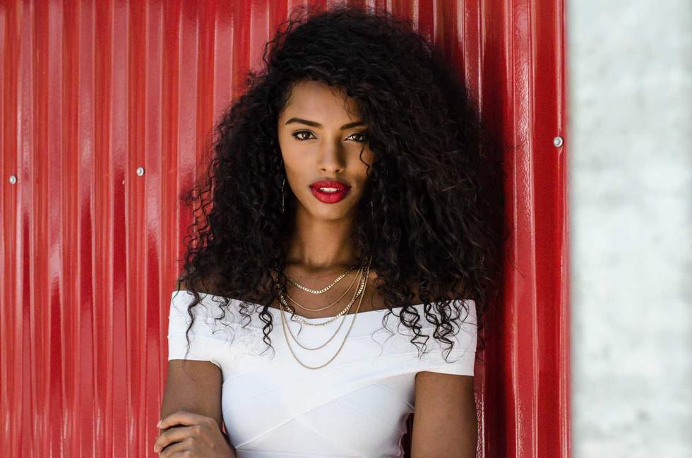 Fashionable black woman with red lips leaning in a red wall posing on the street while looking at camera