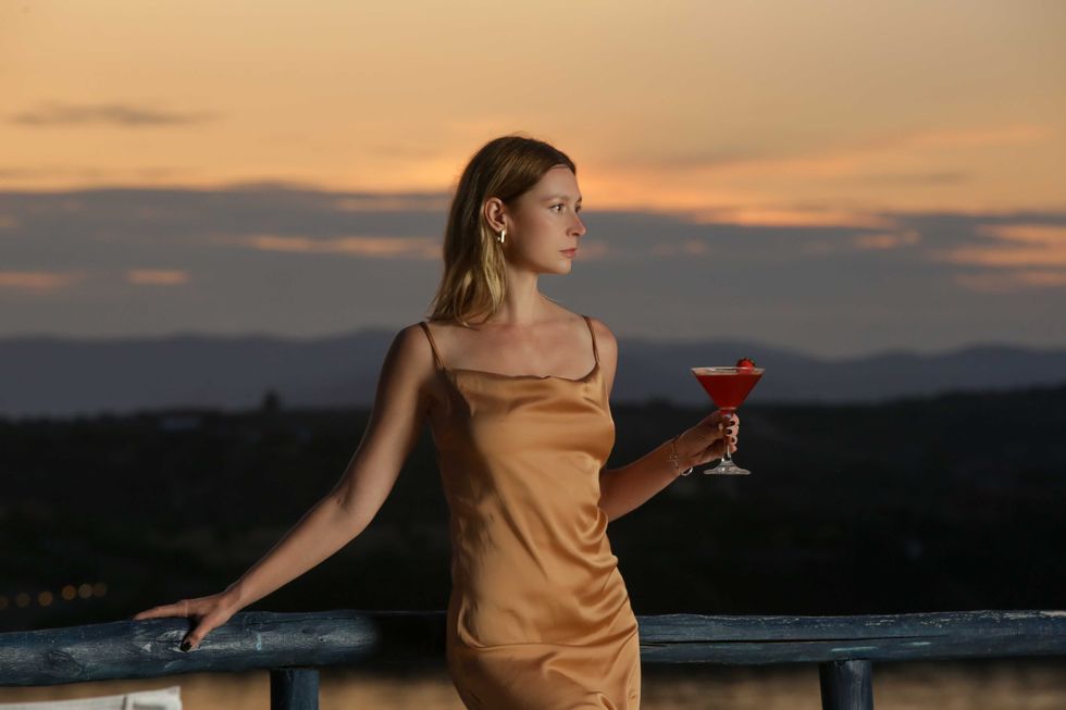 Fashionable young woman holding cocktail with beautiful sunset behind