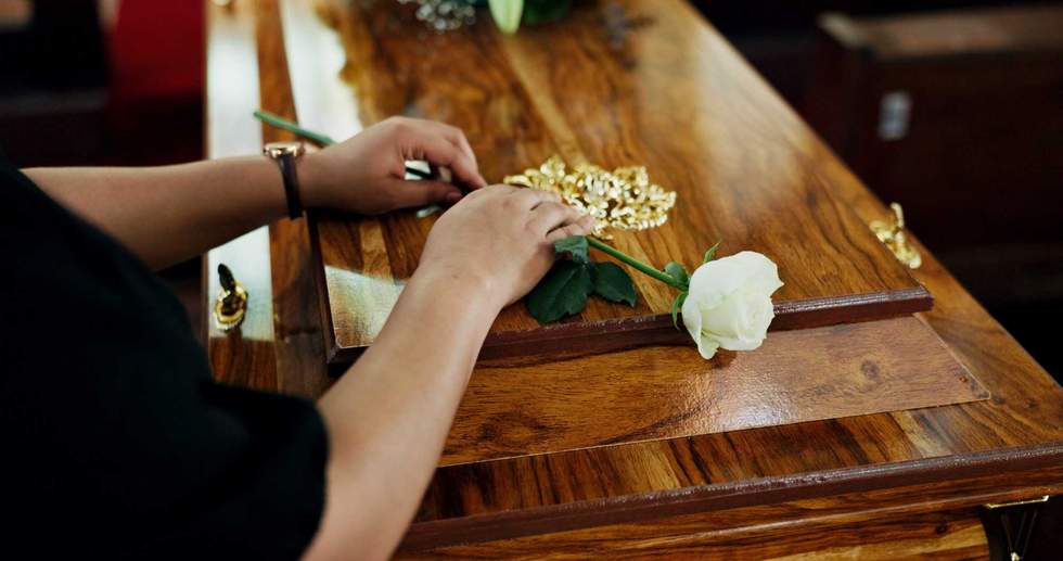 Hands, person and flower on coffin at funeral for farewell, mourning death and goodbye at burial ceremony. Sad, widow and rip with rose for casket respect, memorial service and emotional for loss.