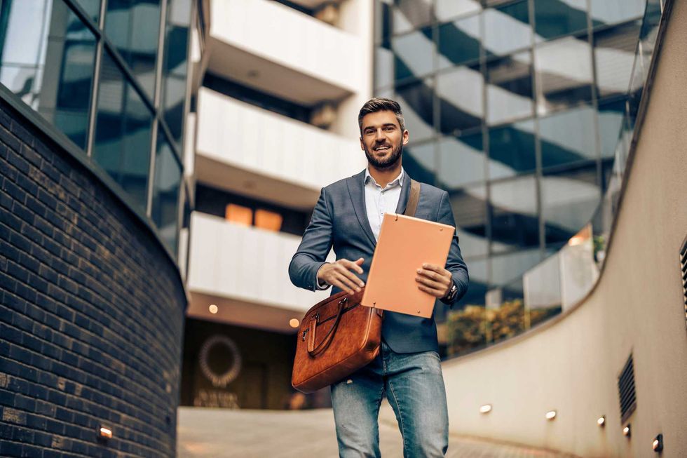 Handsome businessman in corporate suit walking with briefcase in city.