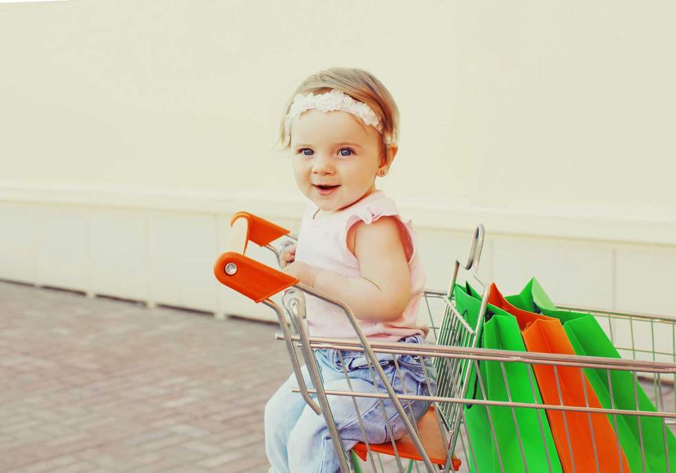 Happy baby with shopping bags sitting in a trolley cart in a city