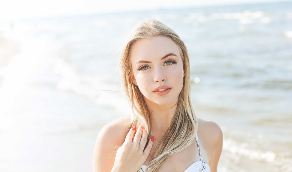Happy blonde woman in free happiness bliss on ocean beach standing straight and posing.