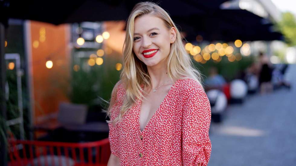Happy young female in trendy dotted garment and with bright makeup smiling and looking at camera while standing on street outside cafeteria in evening