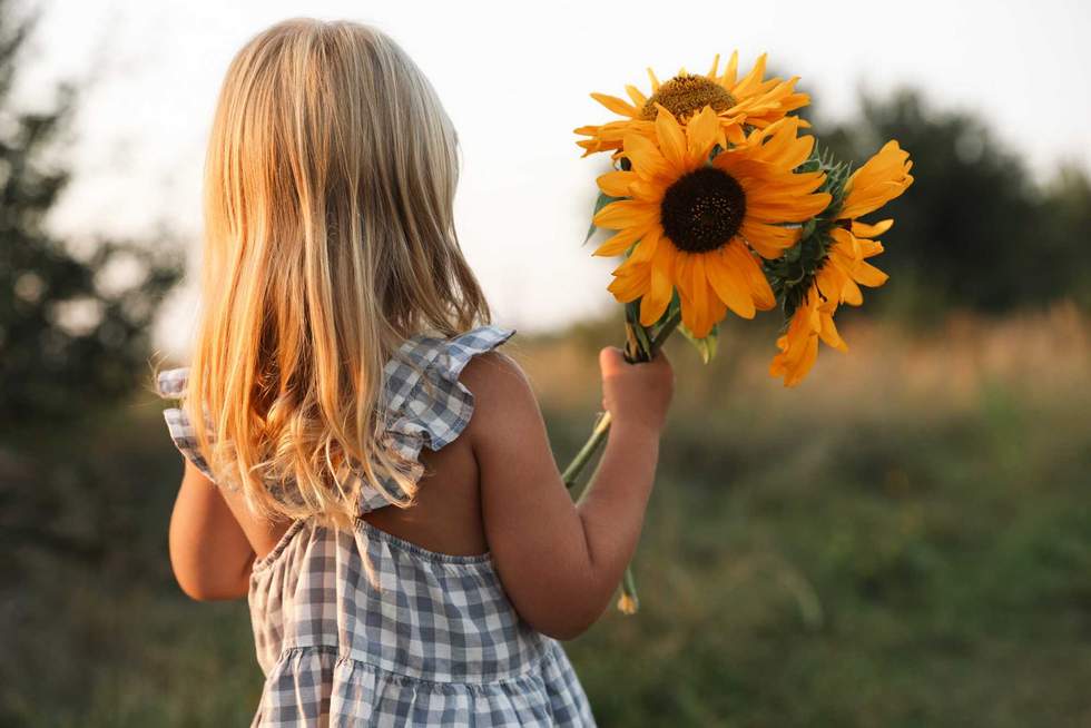 Little girl with sunflowers at meadow, back view. Child enjoying beautiful nature