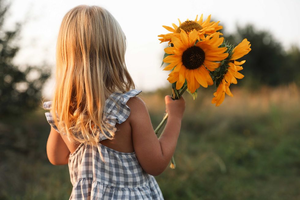 Little girl with sunflowers at meadow, back view. Child enjoying beautiful nature